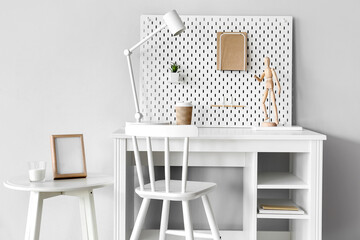 Stylish workplace with different supplies and peg board on grey wall background