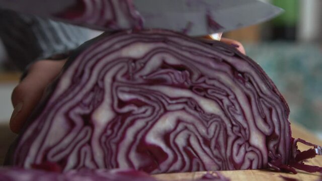 Extreme close up woman's hand ends slicing part of purple red cabbage with a sharp knife in the kitchen. Home cooking and healthy food concept