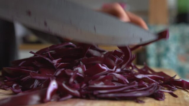 Close up woman's hand gently chopping in pieces Italian purple red cabbage with a rounded sharp knife in the kitchen. Home cooking and healthy food concept