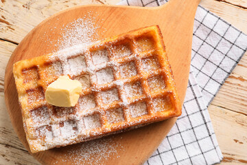 Board with delicious Belgian waffle and butter on light wooden background