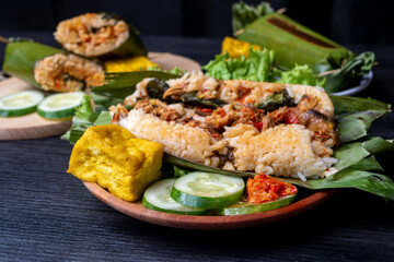 Fototapeta na wymiar Nasi Bakar, Indonesian traditional food, filled with sliced chicken, decorated with cucumber, fried tofu, and chili sauce