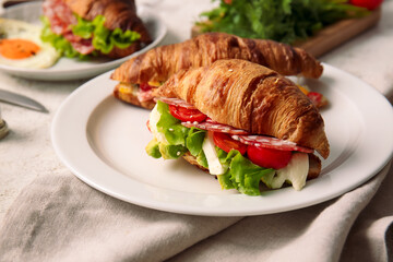 Plate with delicious croissant sandwiches on light background