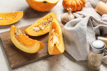 Wooden board with fresh pumpkin pieces on light background