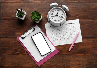 Top view of smartphone, calendar, alarm clock and succulents on wooden background