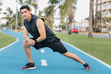 Hispanic young adult man stretching his legs before doing exercise at a park