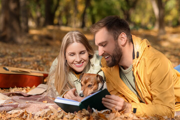 Lovely couple with Jack Russel terrier reading book in park on autumn day