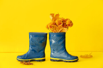 Rubber boots with flowers and fallen leaves on yellow background