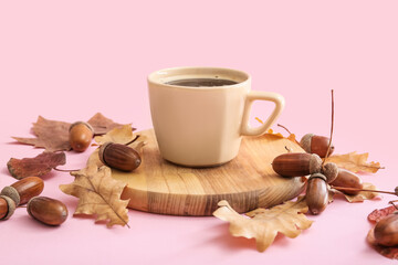 Cup of coffee with acorns and autumn leaves on pink background