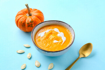 Bowl with delicious pumpkin cream soup and seeds on blue background