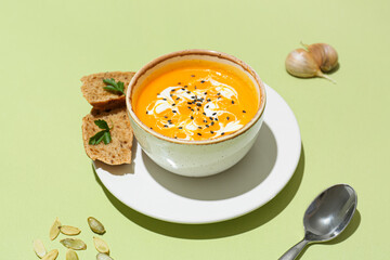 Bowl with delicious pumpkin cream soup and seeds on color background