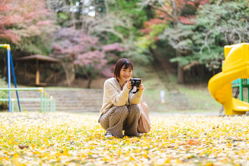 紅葉の公園でカメラを持って写真を撮る女性