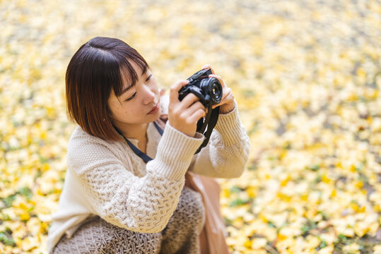 紅葉の公園でカメラを持って写真を撮る女性
