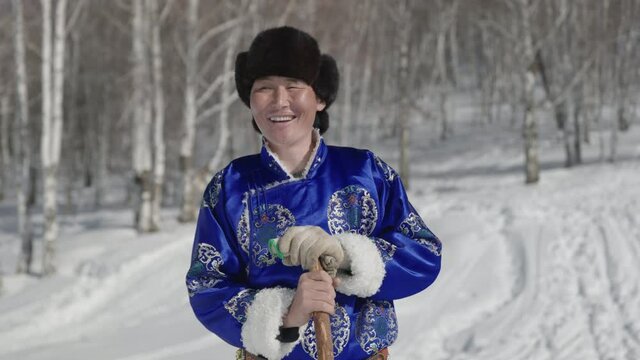 Confident Mongolian man dressed in traditional deel standing outside in snow.