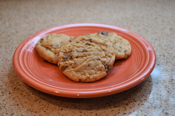 Close-up of three homemade chocolate chip cookies on an orange plate
