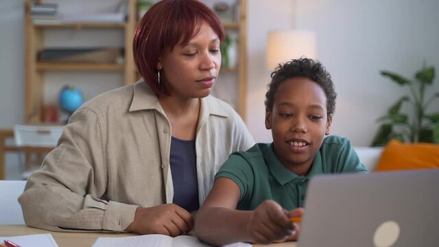 Online education at home. Pretty African-American brunette woman cheers up little son student doing complicated homework at online lesson in room spbd