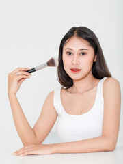 Portrait beauty studio shot of millennial Asian short black hair female model in tank top vest undershirt place arm on table holding concealer brush in hand look at camera on white background