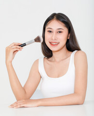 Portrait beauty studio shot of millennial Asian short black hair female model in tank top vest undershirt place arm on table holding concealer brush in hand look at camera on white background