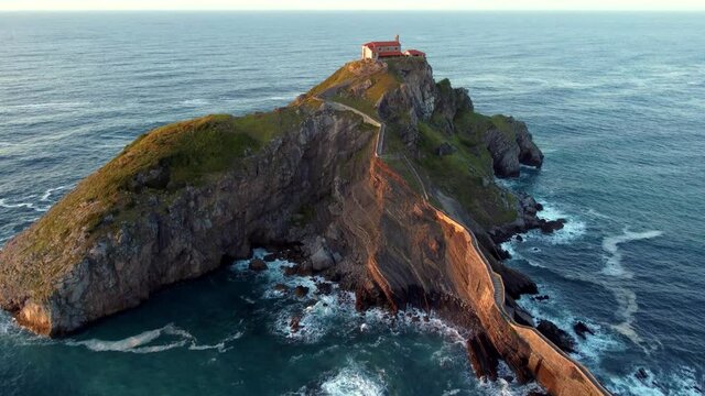 Islet of Gaztelugatxeko surrounded by incredible waves of the Atlantic ocean that crash on its rocky shore. San Juan de Gaztelugatxe church stands in glory and beauty over the water. Shot in 4k.