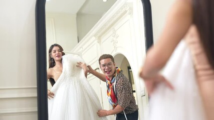 4K Asian LGBTQ guy bridal shop owner helping female bride customer choosing and trying on wedding gown at wedding studio. Small business entrepreneur wedding planner and marriage ceremony concept