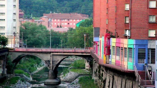 static shot of a bridge in Basauri with beautiful colors due to a graffiti that illuminates it while the bridge shows an estuary and buildings on both sides of the road and the estuary