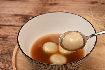 Close up rice dumpling balls with sweet ginger soup in ceramic bowl.