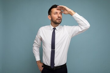 Photo of positive self-confident young handsome brunet unshaven male business man with beard wearing casual white shirt and tie isolated over blue background with copy space for text and looking for