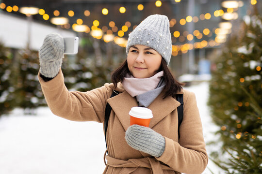 Happy woman in winter wear with coffee doing selfie in christmas market