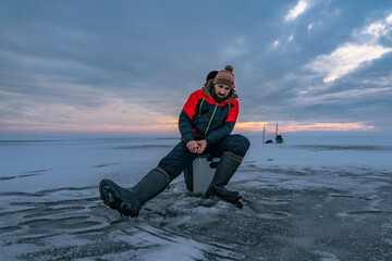 Winter ice fishing. Fisherman on lake catc fish from snowy ice