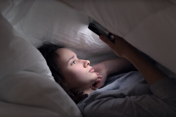 young woman uses smartphone in bed at night before bedtime