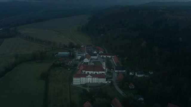 Tilt up reveal drone shot from a bavarian monastery uo to the violett bright horizon sunset view with the alps in the background