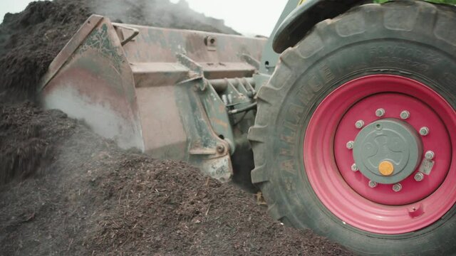 Close up of a wheel loader driving towards a compost heap loading his shovel.