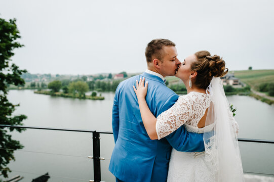 The bride and groom kiss on wedding ceremony on pier. A newlyweds couple in a country. Photo near lake outdoors.