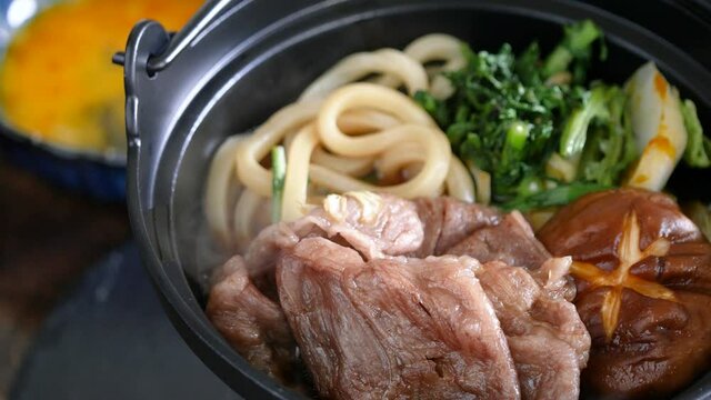 すき焼きの動画。小さい鍋で煮込んでる牛肉とうどん。