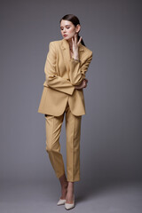High fashion photo of a beautiful elegant young woman in a pretty  beige sand suit, jacket, pants, trousers, accessories posing on gray background. Studio Shot. Slim figure.