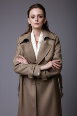 High fashion photo of a beautiful elegant young woman in a pretty dark beige, brown suit, accessories, white handbag posing on gray background. Studio Shot. Slim figure.