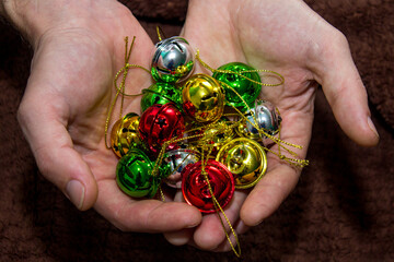 Multi-colored jingle bells in men's hands. Selective focus. Dark background. Close-up