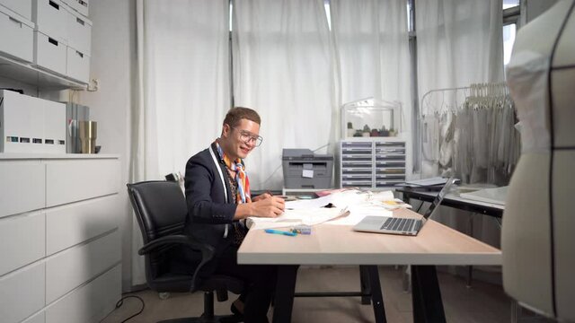 4K  Smiling Asian LGBTQ guy bridal shop owner working and making wedding dress sewing pattern in office room at wedding studio. Small business entrepreneur wedding planner and tailor designer concept