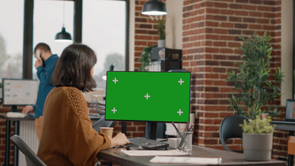 Employee looking at horizontal green screen on computer display at desk. Woman using monitor with...