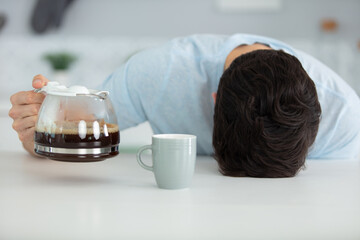 sleepy man pouring coffee into cup at home in morning