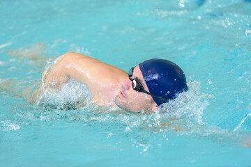 swimmer in glasses swims in indoor swimming pool