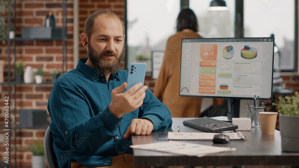 Poster employee holding smartphone to talk on video call with colleagues in startup office. business man us