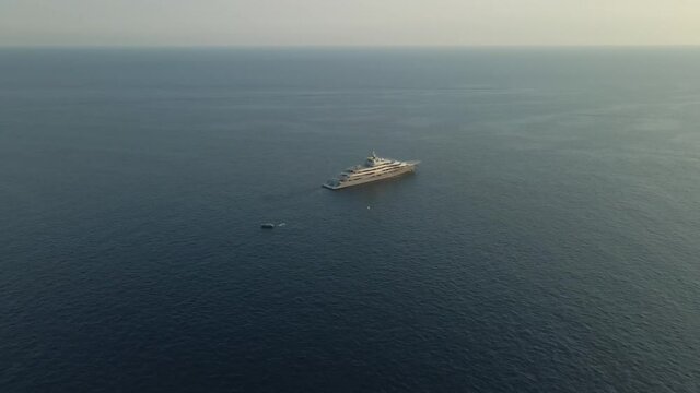 drone footage of mega yacht in middle of ocean with tender boat off back midday