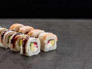 Japanese Unagi Ebi sushi roll with avocado and cream cheese inside roll. Asian dish pieces with eel, shrimp slices on top served with sauce, dark concrete background. Single object. Inside out sushi
