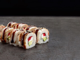 Japanese Unagi sushi roll with avocado and cream cheese inside roll. Asian dish pieces with eel on top served with sauce, dark concrete background. Copy space image. Single object. Inside out sushi
