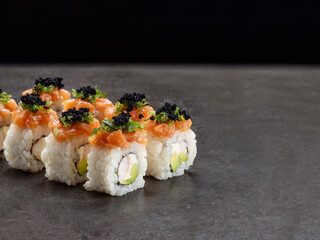 Japanese Ebi sushi roll with shrimp (prawn), avocado and cream cheese inside roll. Asian dish pieces with salmon on top on dark concrete background. Copy space image. Single object. Inside out sushi
