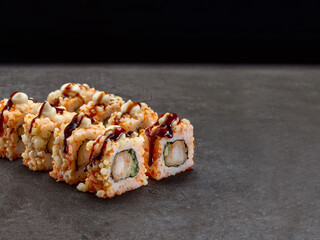 Crunchy Japanese sushi roll with tempura shrimp, cucumber inside roll. Asian dish pieces served with sauce on dark concrete background. Copy space image. Single object. Inside out sushi
