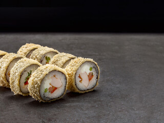 Japanese crunchy sushi roll in fried tempura with smoked chicken breast, tomato, spring onion, cream cheese inside roll. Asian dish pieces on dark concrete background. Copy space image. Single object

