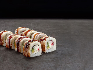 Japanese Unagi sushi roll with crab meat sticks, avocado, cream cheese inside roll. Asian dish pieces with eel on top served with sauce on concrete background. Single object. Inside out sushi
