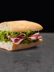 Italian Ciabatta bread sandwich with ham slices, cheese and fresh lettuce served without plate on...