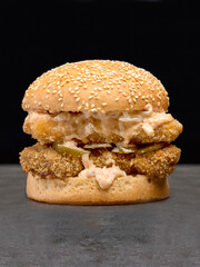 Crispy chicken nuggets burger in wheat Bun with sesame seeds isolated on dark stone background....